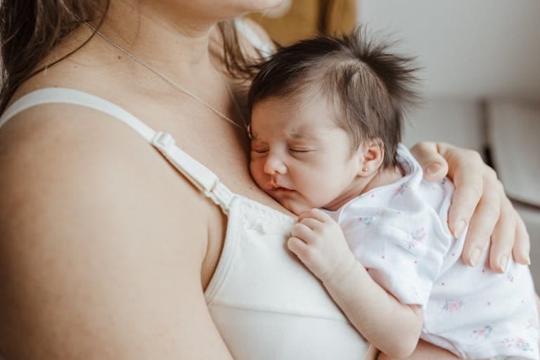 A mother holds her sleeping newborn close, showcasing love and bonding indoors.