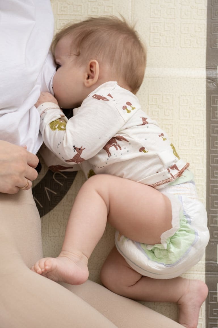 From above of crop unrecognizable caring mother lying near adorable barefoot newborn baby in diaper in light room at home