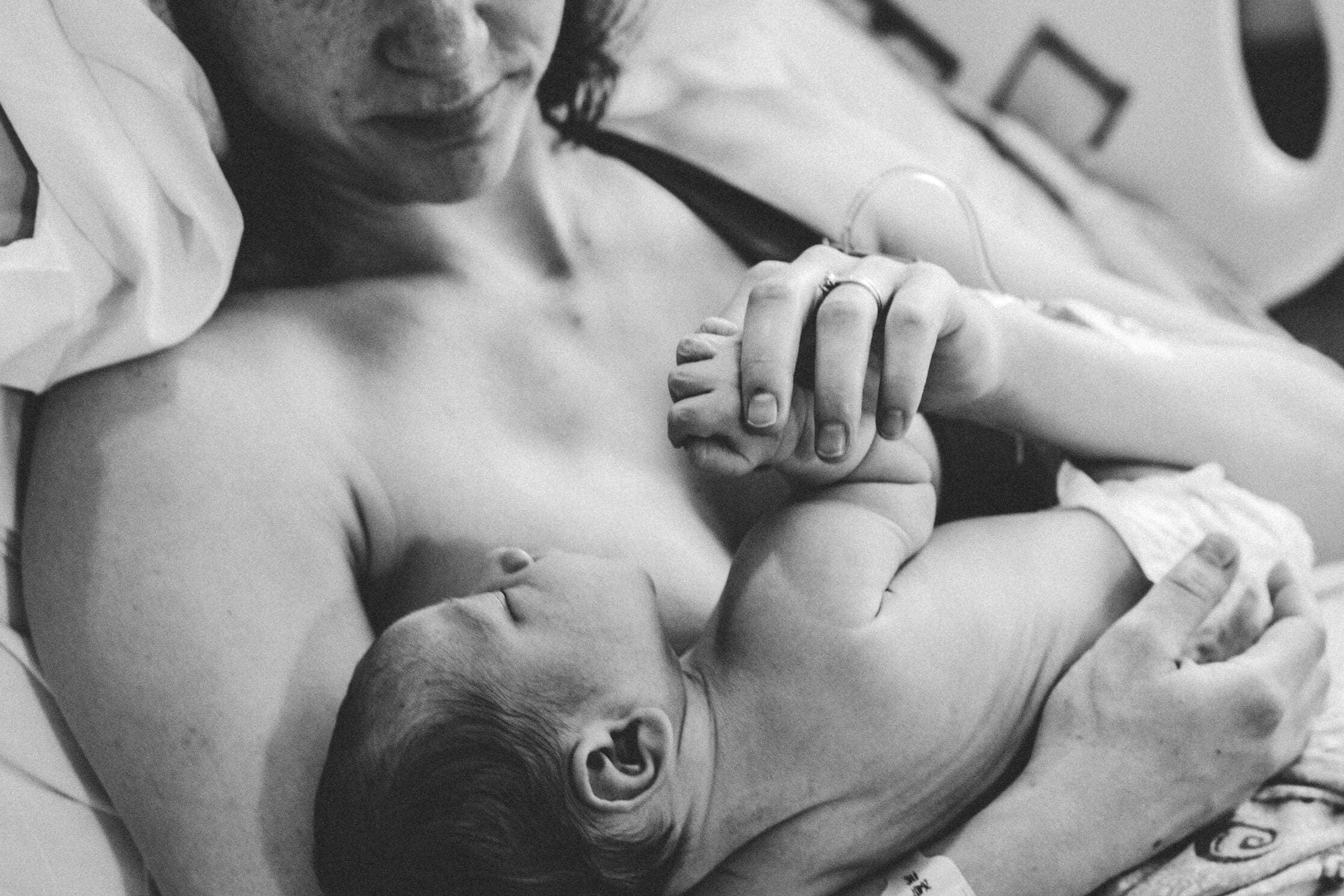 Black and white image capturing a tender moment between a mother and her newborn in a hospital setting.